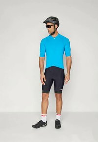 Modrý cyklistický dres s krátkým rukávem, černé šortky s vložkou, černé cyklistické boty, bílé a červené pruhované ponožky, černá helma a sluneční brýle.