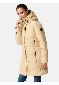 Chaqueta de plumas beige con cuello alto, cremalleras y detalle del logo en la manga. Textura acolchada y longitud ligeramente mayor para mayor calidez.