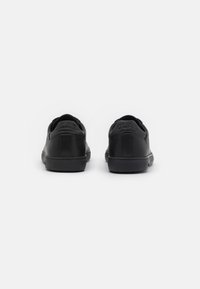 Black leather sneakers featuring a smooth finish, round toe, textured sole, and embossed branding on the heel and back panel.