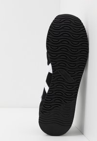 Black sneaker outsole with a wavy pattern, featuring a textured surface. Materials include rubber and mesh. Each side has white accents.