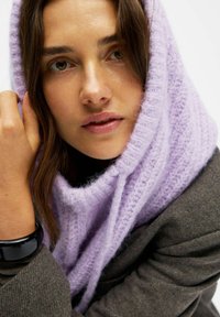 Sciarpa di maglia viola chiaro con una texture morbida, che si drappeggia liberamente attorno al collo. Indossata con un blazer scuro e strutturato.
