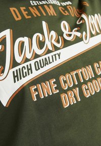 Roheline puuvillane T-särk, millel on valged ja oranžid tekstid, sealhulgas "Jack & Jones," "Kõrge Kvaliteet" ja "Peen Puuvillane Hooldus."
