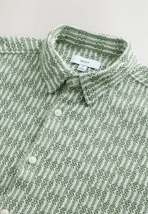 Green and white zigzag patterned shirt with a collared neckline, button closures, and a soft, textured fabric. Brand label visible.