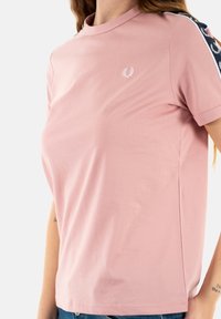 Rosa kortärmad t-shirt med rund hals, prydd med en vit logotyp på bröstet och marinblå detaljer längs axlarna.