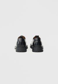 Schwarze Lederschuhe mit rundem Design, ausgestattet mit einer dicken Gummisohle und Akzentnähten. Enthält einen Tab an der Ferse für ein einfaches Anziehen.