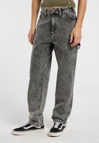 Vaqueros de denim gris con un corte relajado, cintura alta y textura desteñida. Combinados con zapatillas negras con acentos blancos.