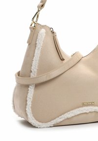 Beige håndtaske med en blød tekstur, der har en shearling-detalje langs sømmene, guldfarvet hardware og en aftagelig skulderrem.