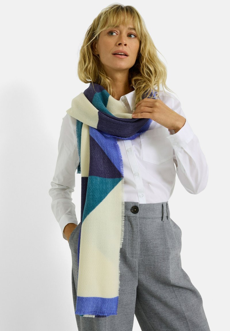 Écharpe en tissu doux à motifs géométriques colorés, présentant des nuances de bleu, teal et crème, avec des bords frangés.