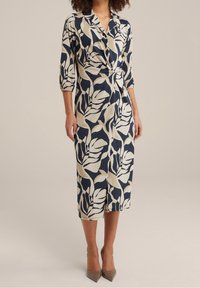 Navy- und cremefarbene Wickelkleid mit Blattdesign, Dreiviertelärmel und einer Schleife an der Taille; knielang mit einem leichten Schlitz vorne.