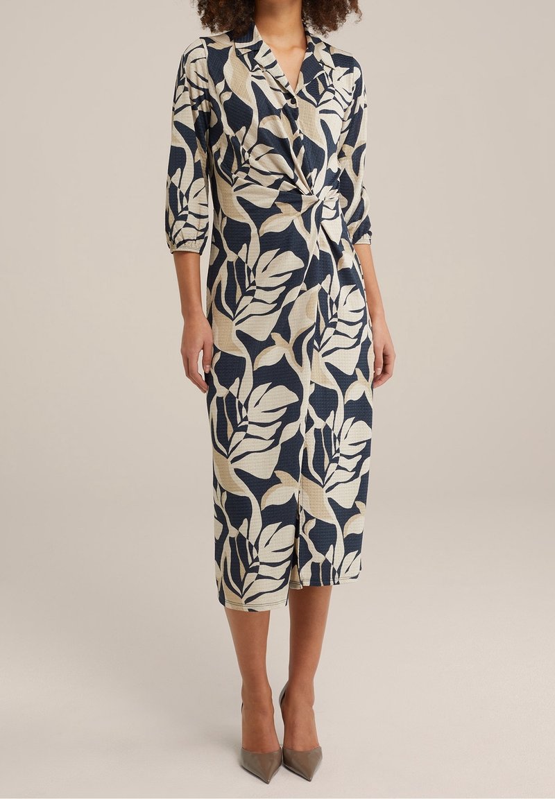 Navy- und cremefarbene Wickelkleid mit Blattdesign, Dreiviertelärmel und einer Schleife an der Taille; knielang mit einem leichten Schlitz vorne.