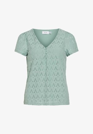 Világoszöld, rövid ujjú blúz V-nyakkivágással, díszgombokkal, és a teljes anyagon lyukacsos rombuszmintával.