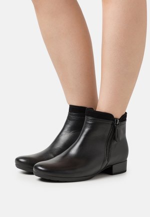 Schwarze Leder-Stiefeletten mit glatter Oberfläche, niedrigem Blockabsatz und einem seitlichen Reißverschluss. Weicher Stoff am Schaft für Komfort und Passform.