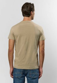 Beige t-shirt med kort ärm, i bomullsmaterial, rundad hals, slät yta, bärs tillsammans med blå jeans, visad från baksidan.