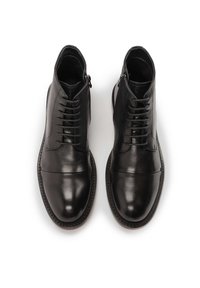 Botas negras de cuero hasta el tobillo con cierre de cremallera en el costado y cordones en la parte delantera. Textura suave con puntera redonda y detalles cosidos.