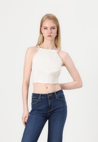 Cream-colored cropped top with a halter neck design and stitch detailing, paired with dark blue high-waisted jeans. Smooth fabric texture.