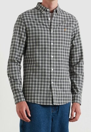 Mann trägt ein schwarz-weiß kariertes Hemd mit Knöpfen, Kragen und langen Ärmeln, kombiniert mit blauen Jeans.