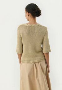 Pull en tricot beige à manches courtes et à col côtelé, avec une coupe ample et un tissu texturé. Porté avec une jupe légère et fluide.