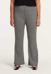 Zwart-witte houndstooth print broeken met een flared model. Gladde stof, hoge taille en gedetailleerde stiksels. Gepaard met zwarte schoenen.