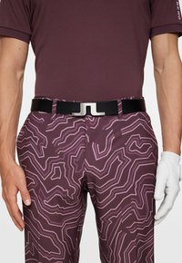 Golfowy strój z bordową koszulą w wzory oraz spodniami w fioletowy abstrakcyjny wzór. Czarny pasek ze srebrną klamrą. Biała rękawiczka.