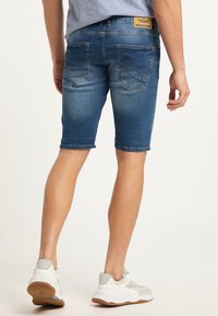 Shorts de mezclilla en un tono azul medio con un diseño ajustado, que cuentan con bolsillos traseros y dobladillos deshilachados. Combinados con zapatillas deportivas ligeras.