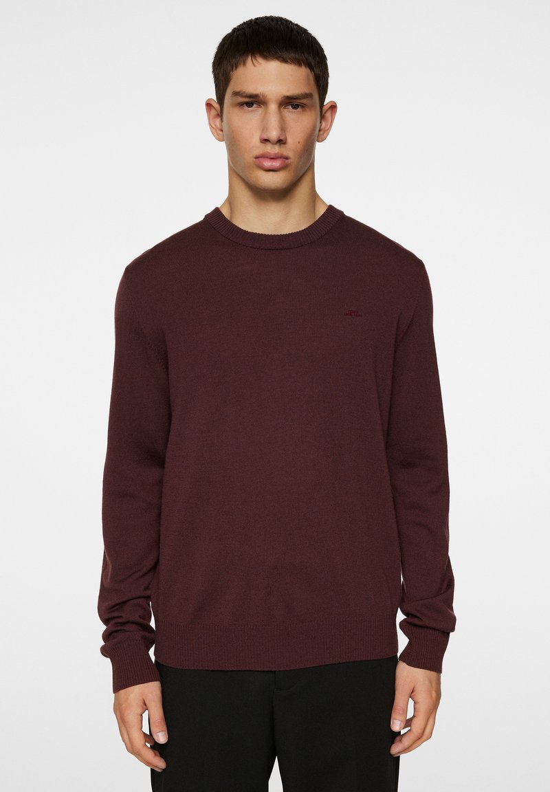 Bordeaux gebreide trui met een ronde hals, lange mouwen en geribbelde zoom. Kenmerkt zich door een subtiel logo op de borst en een soepele textuur.