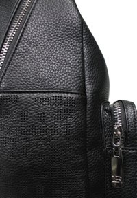 Zaino in pelle nera caratterizzato da un materiale texturizzato, dettagli con zip e un motivo perforato sul pannello frontale.