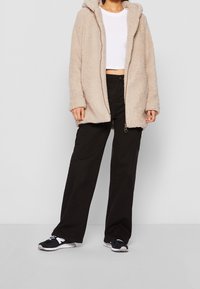 Felpa beige foderata in pile con vestibilità comoda, dotata di apertura frontale e tasche laterali, abbinata a pantaloni neri a gamba larga e sneaker neri.
