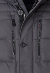 Giacca a vento grigia con una texture liscia, dotata di due tasche con zip, una chiusura a bottone e un colletto foderato.