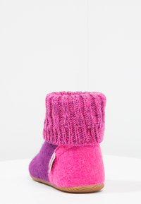 Filcowe kapcie z złożonym dzianinowym mankietem, w odcieniach różu i fioletu, o okrągłym kształcie i teksturowanej powierzchni. Gumowa podeszwa dla lepszej przyczepności.