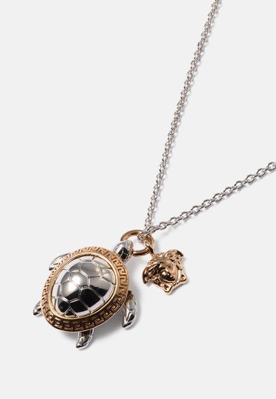 Colar com pendente de tartaruga em tom prateado e dourado, apresentando uma concha decorada e um charme de leão numa corrente de metal torcida.