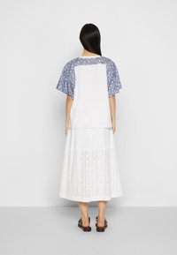 Camiseta blanca con mangas de estampado floral azul, combinada con una falda blanca de longitud a la rodilla con patrones de ojal y un diseño en capas.