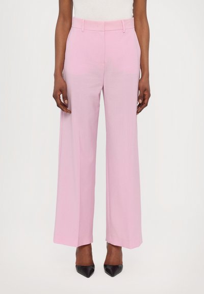 Rosa weite Hose mit glatter Textur, hohem Bund und Gürtelschlaufen, kombiniert mit spitzen schwarzen Absätzen.