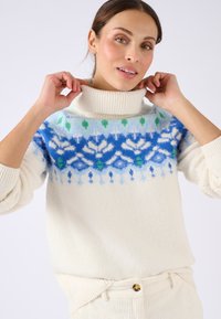 Maglione bianco a collo alto con motivo Fair Isle blu, verde e bianco sul petto; tessuto testurizzato con colletto e polsini a costine.
