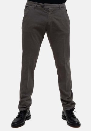 Pantaloni di cotone grigi con una vestibilità slim, dotati di tasche anteriori e chiusura con zip. Indossati con scarpe eleganti nere per creare contrasto con lo sfondo chiaro.