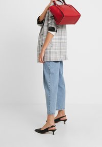 Rote rechteckige Handtasche mit abgerundeten Ecken, glattes Leder, kombiniert mit einem karierten Blazer, hellblauen Jeans und schwarzen Slingback-Schuhen.
