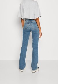 Jeans azules acampanados con cintura alta, con detalles de costura y dos bolsillos traseros, combinados con una camiseta corta gris.