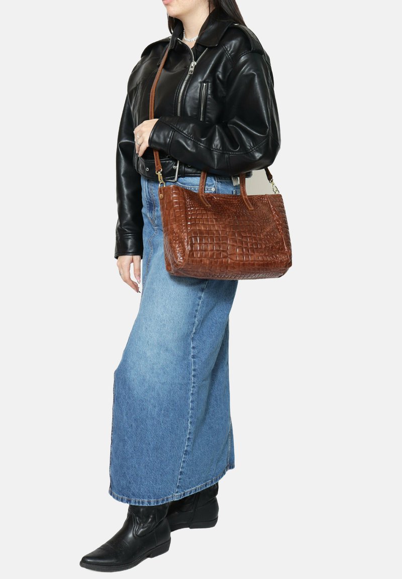 Borsa a tracolla in pelle marrone con texture e motivo coccodrillo, dotata di manici corti e una lunga tracolla, presentata insieme a un modello.