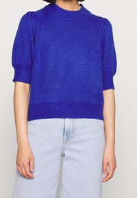 Lila stickad kortärmad tröja med ribbat halslinning och puffärmar, kombinerad med ljusblå högmidjade jeans.