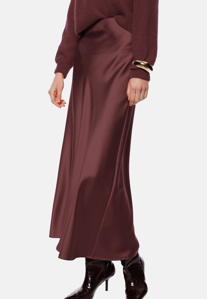 Gonna lunga in satin bordeaux con una texture liscia, design fluido e leggero lucido, abbinata a stivaletti neri lucidi con tacco alto.