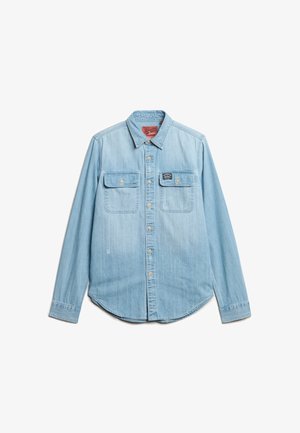 Lyseblå denimskjorte med lange ærmer, to brystlommer og en spids krave. Har metalknapper og en rund kant.