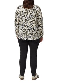 Lange mouw top in crème met zwart en tan luipaardprint, gecombineerd met zwarte broek en lichtgekleurde, casual schoenen.