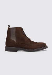 Botín de ante marrón con cierre de cordones, que presenta un diseño de brogue y paneles laterales de tela. Suela de goma resistente.