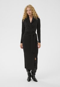 Juodas kepurinis su giliu V formos iškirpimu, ilgomis rankovėmis ir juosmeniu aprišimo dirželiu. Yra šoninė skeltukas ir minkšta, tampri medžiaga. Kelio ilgio juodi batai.