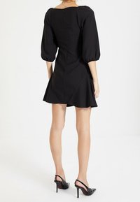 Vestido negro con un cuerpo ajustado y un dobladillo acampanado, que cuenta con mangas abullonadas y un escote cuadrado. Textura suave con un cierre de cremallera en la parte posterior.