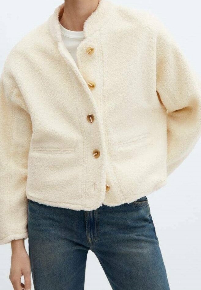 Veste duveteuse couleur crème avec un col rond, dotée d'une fermeture avant avec des boutons dorés et deux poches latérales.