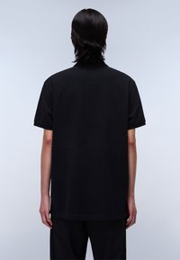 Svart kortärmad skjorta med avslappnad passform och mjuk textur. Rak nederkant och minimalistisk design. Bärs med svarta byxor.