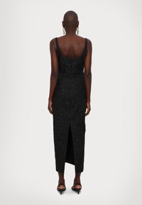 Schwarzes Kleid mit Spaghetti-Trägern, strukturierter Stoff, figurschnitt und einem seitlichen Schlitz, der bis zur Mitte der Wade reicht. Reißverschluss im Rücken.
