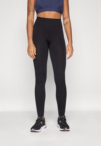 Czarne legginsy z wysokim stanem, prążkowane, o dopasowanym kroju, w połączeniu z czarno-różowymi butami sportowymi.