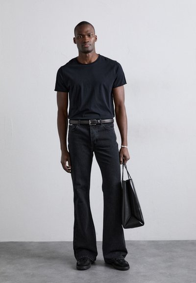 Camiseta de algodón negra, jeans holgados de mezclilla negros acampanados, y bolso de cuero negro con acabado mate. Diseño sencillo sin patrones visibles.