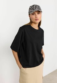 Sort oversized T-shirt med korte ærmer, lavet af bomuld, parret med en beige nederdel. En cap med leopardprint tilføjer mønster og kontrast.